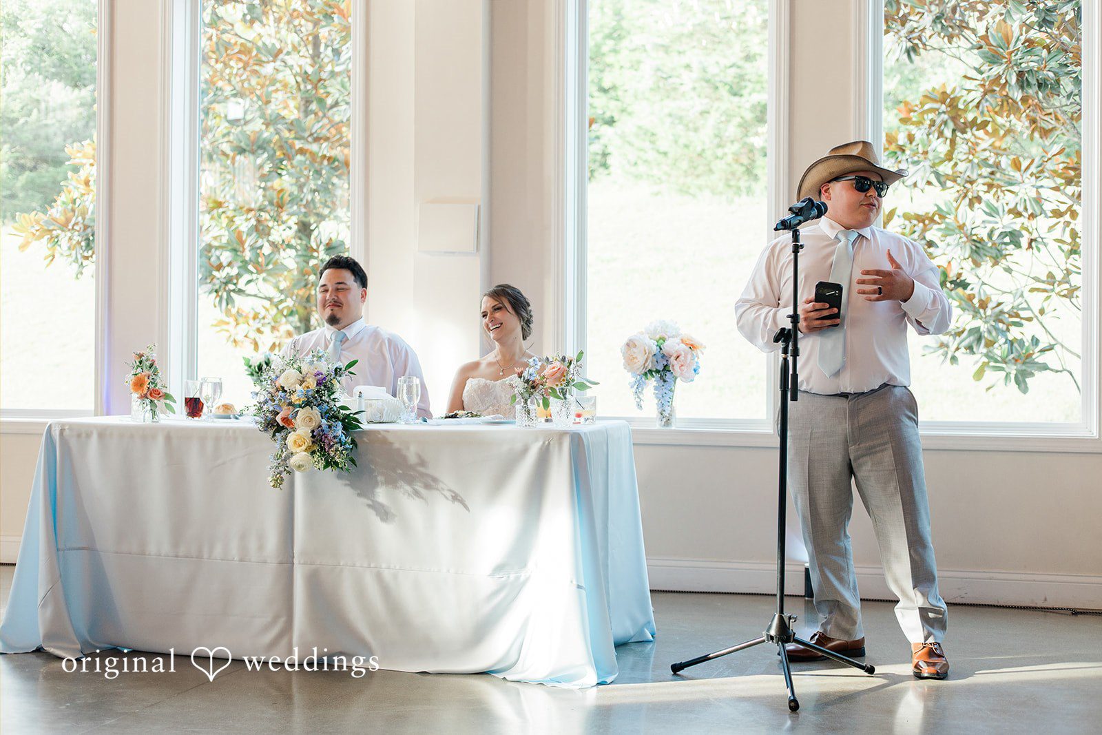 Alexander + Annalisse A speaker stands at a microphone during the reception toasts with the head table nearby.