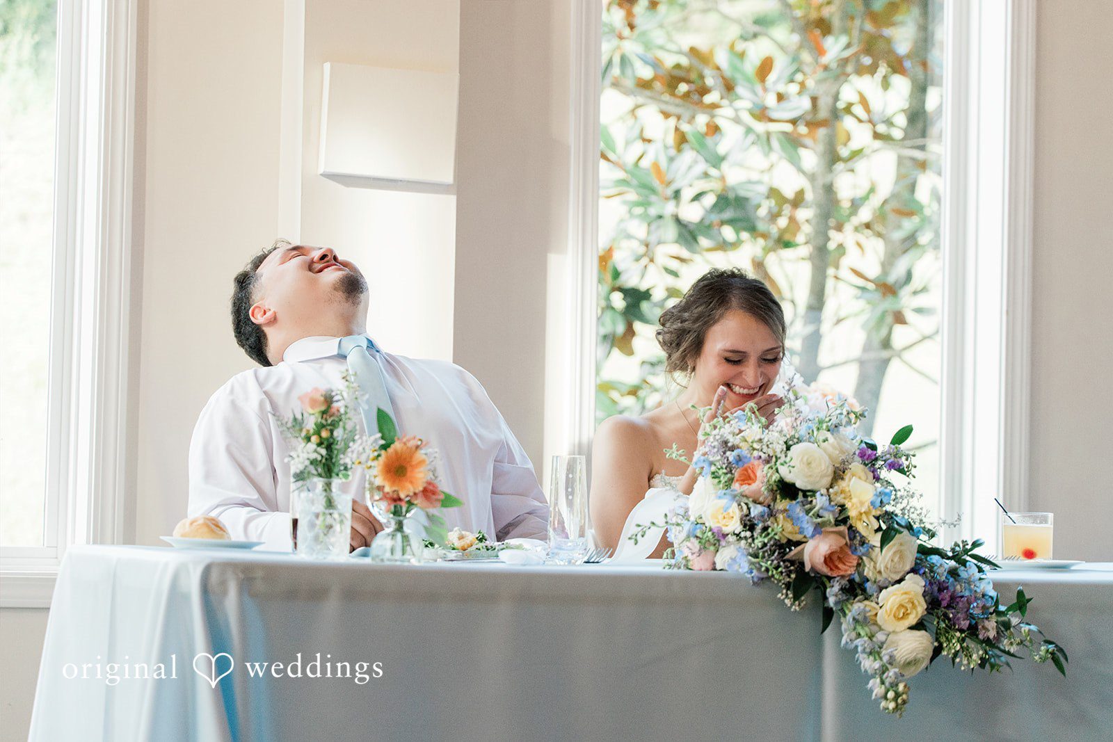 Alexander + Annalisse The newlyweds sit at a decorated head table while looking back over their shoulders.