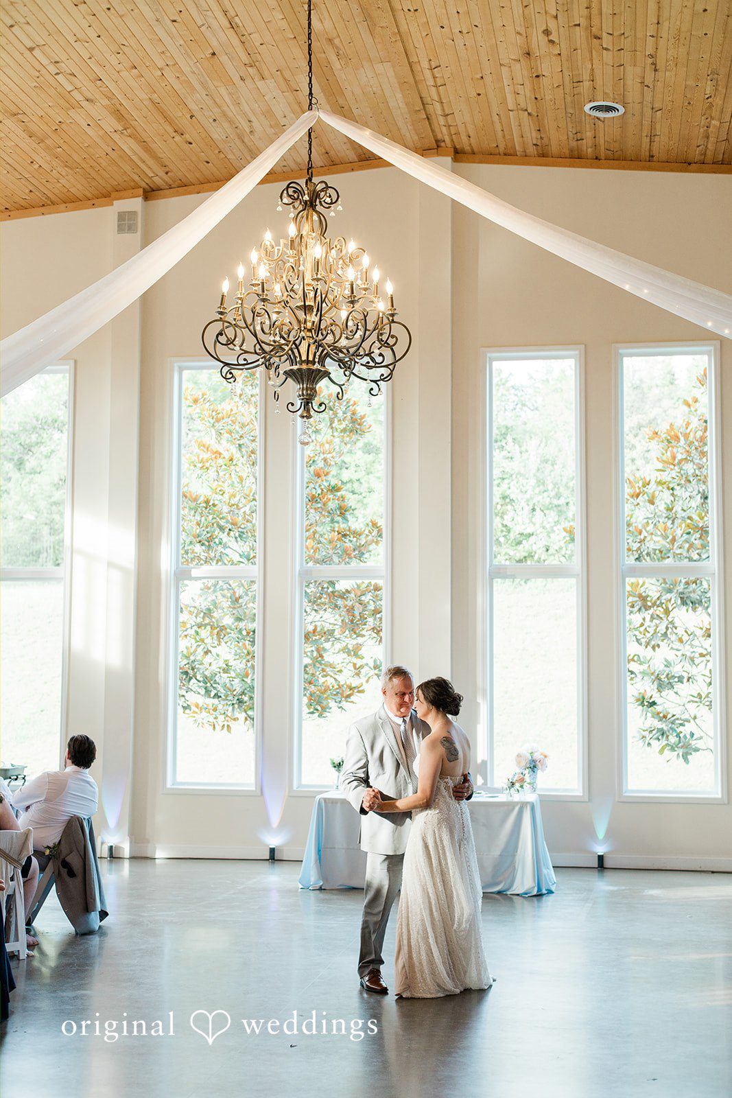 Alexander + Annalisse The newlyweds share a dance under an elegant chandelier in a brightly lit hall.