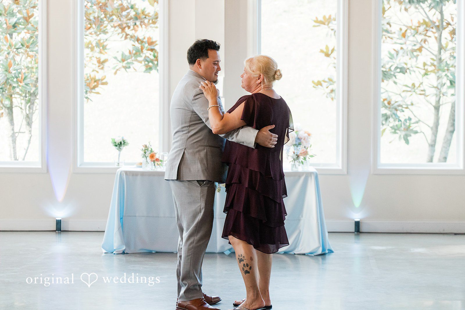 Alexander + Annalisse A groom dances with a guest in a dark dress near a window during the reception.