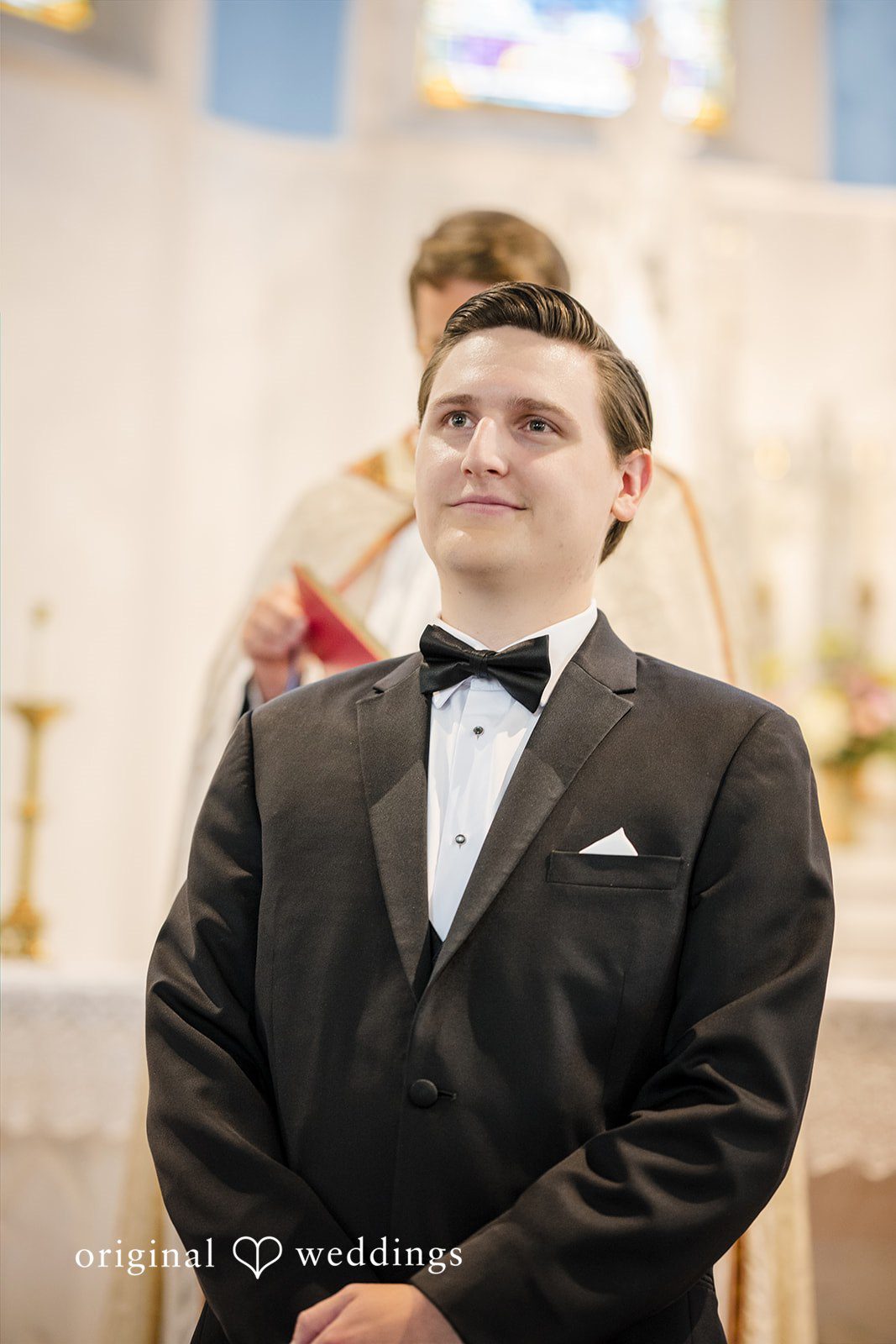 Nicole + Matt A groom in a tuxedo smiling and adjusting his bow tie during a wedding shoot.