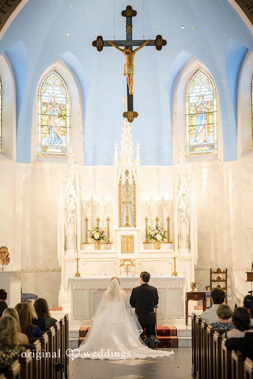 Nicole + Matt A church altar decorated with white flowers under a large wooden wall cross.