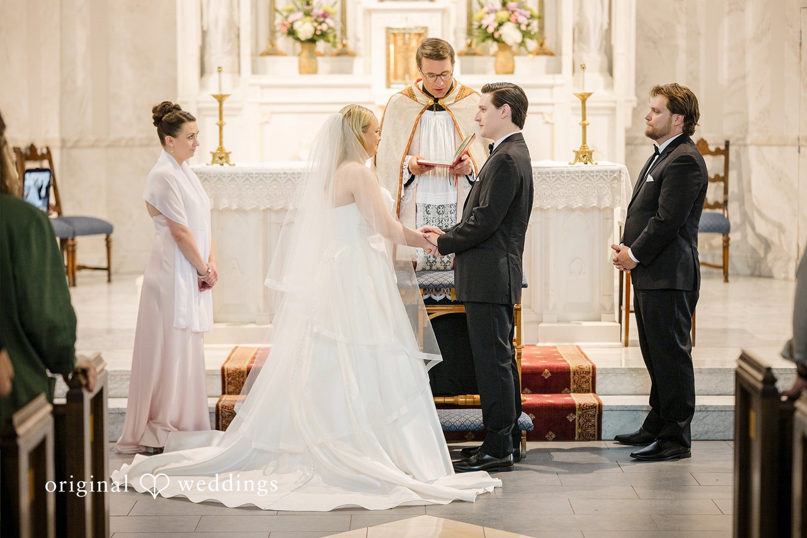 Nicole + Matt A bride and groom exchanging vows at the altar in front of their wedding party.