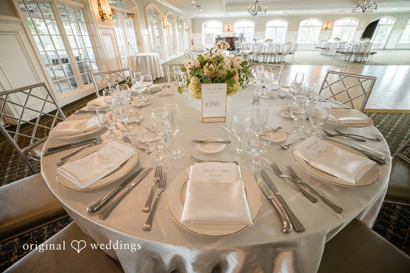 Nicole + Matt A round reception table set with white tableware, glassware, and a central floral arrangement.