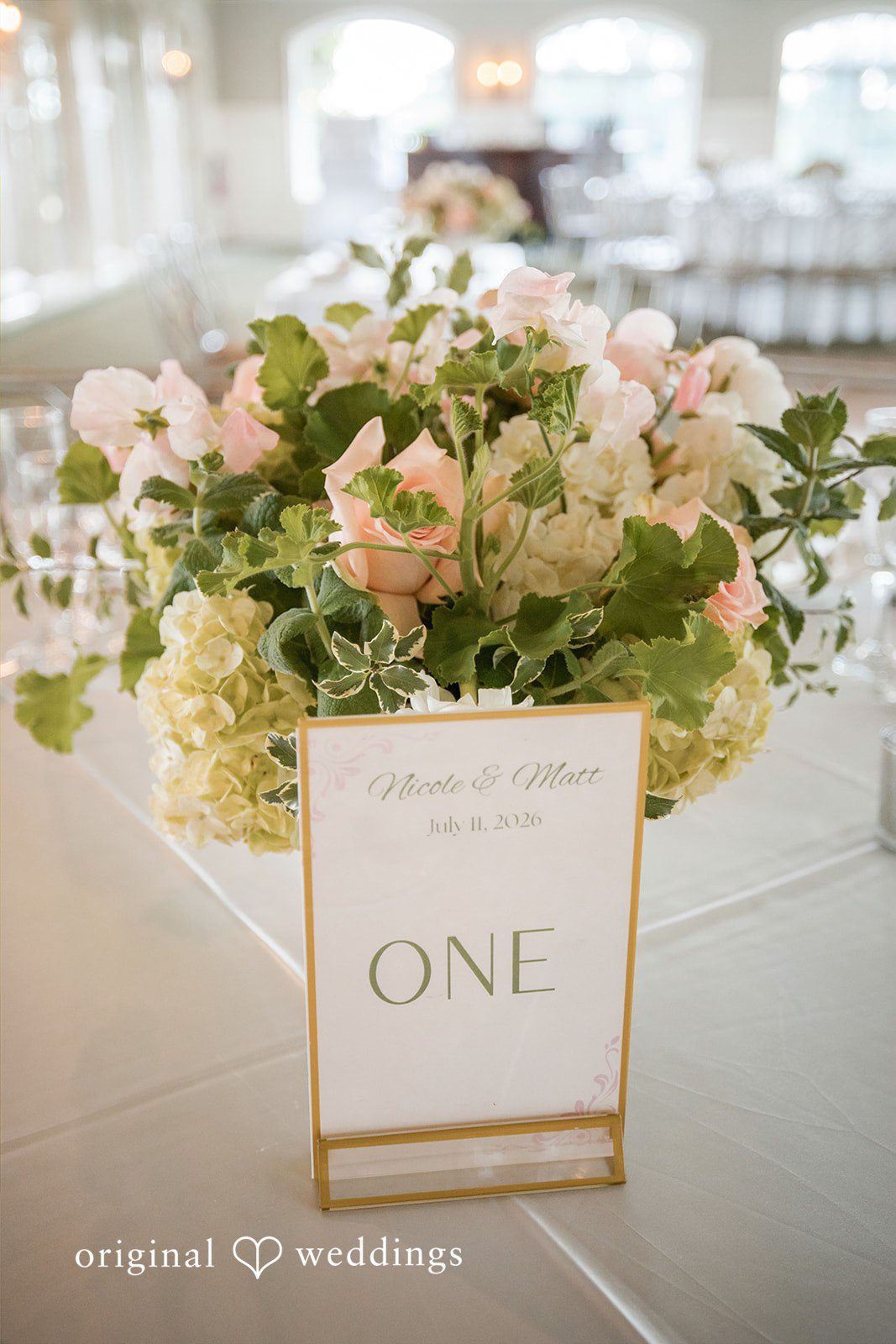 Nicole + Matt A close-up of a white and green floral center table arrangement next to a table number card.