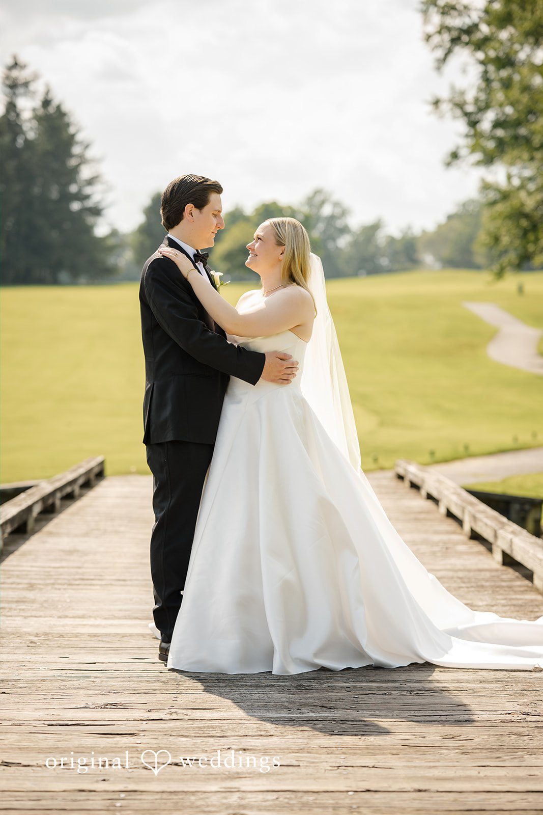 Nicole + Matt A groom embracing his bride on a wooden dock next to a field.