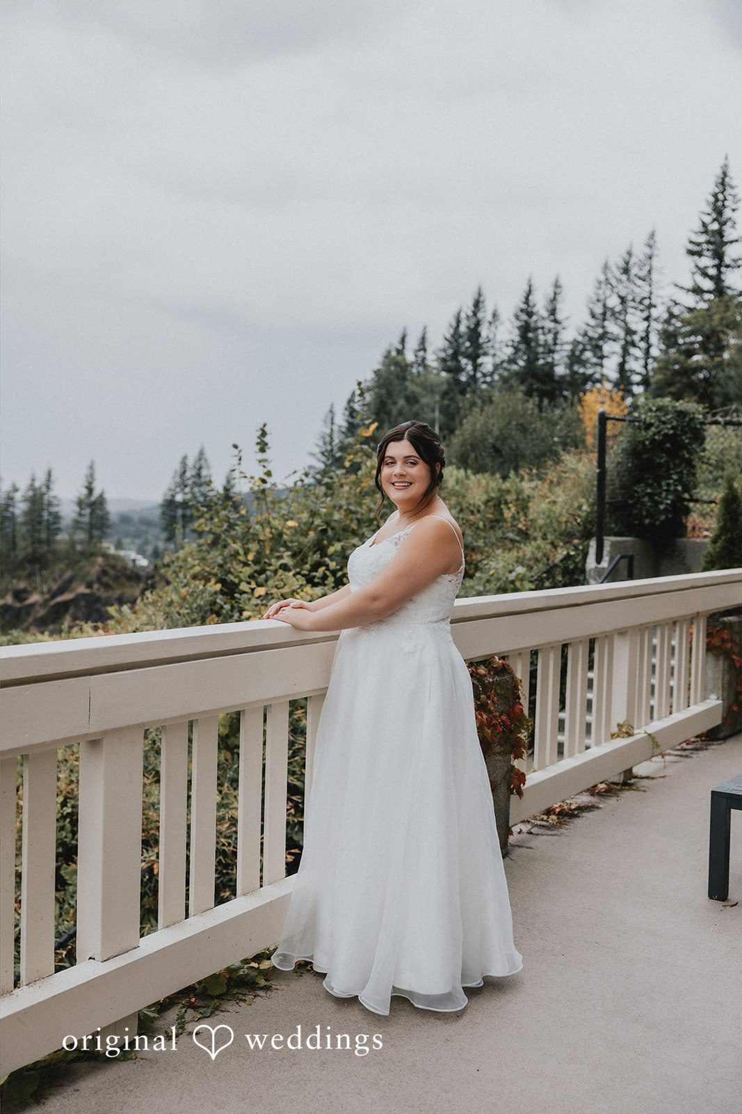 A bride standing on a stone balcony overlooking a forested landscape.