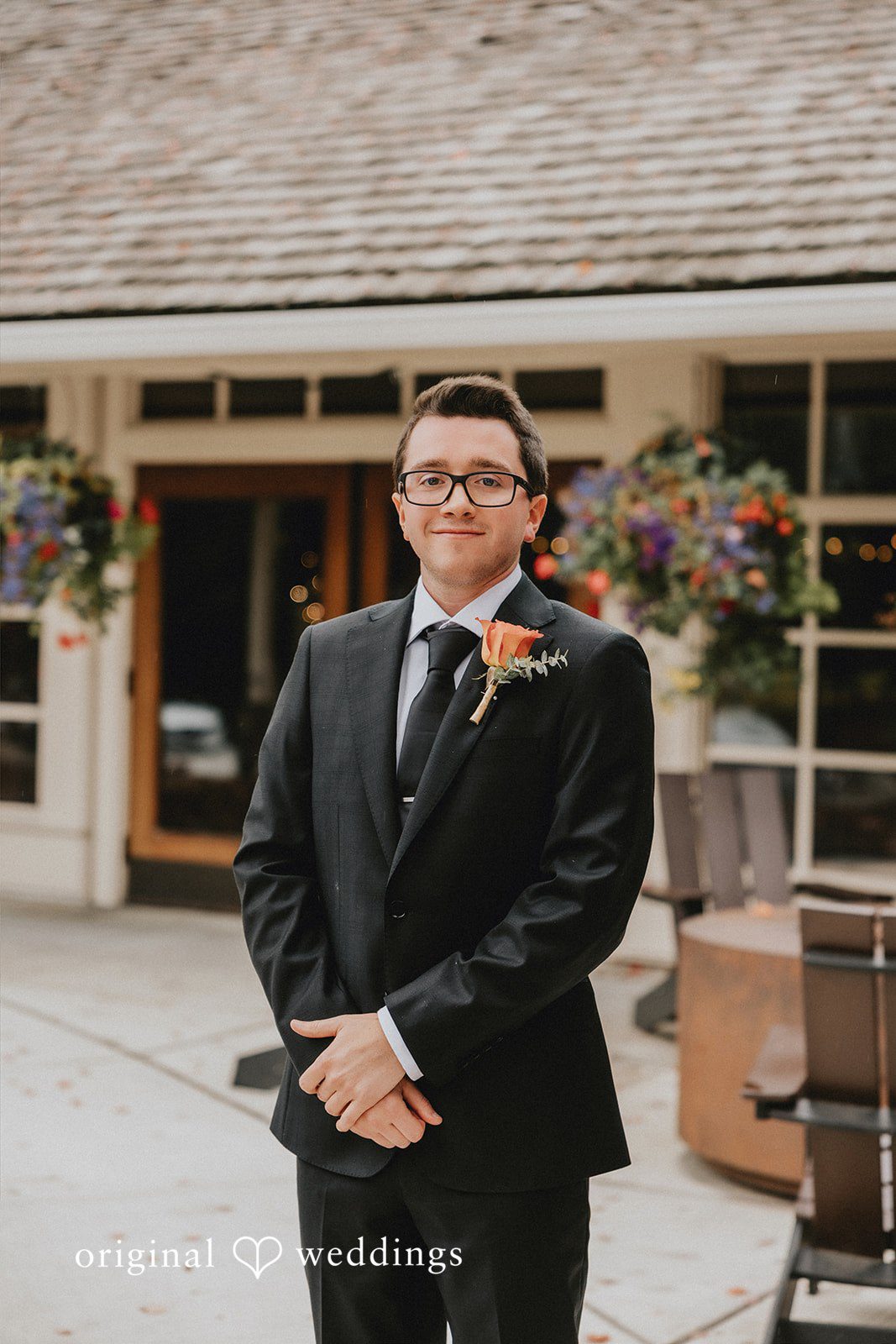 A groom in a black suit smiling while standing in front of a building.