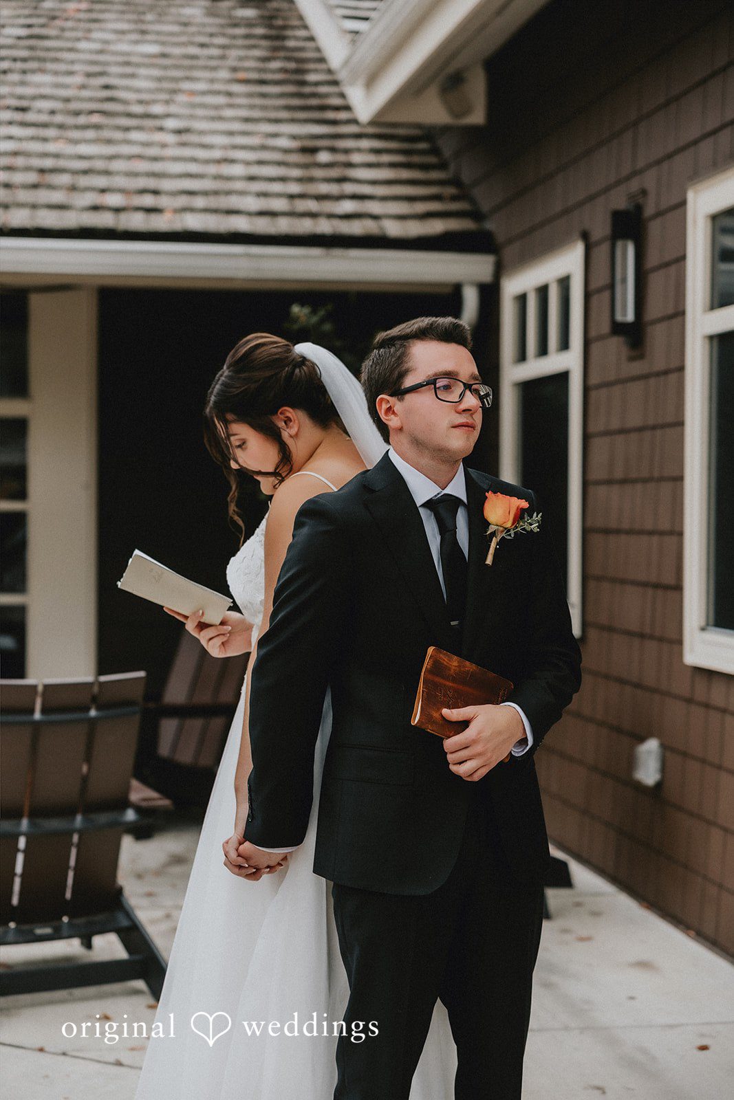 A bride and groom standing near a rustic house during their wedding day.