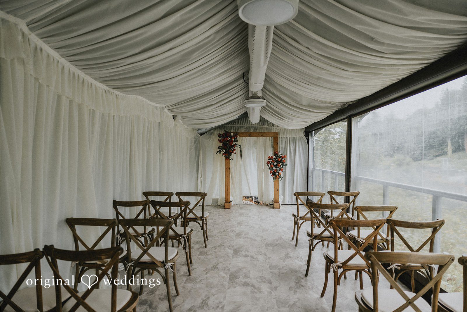 Rows of wooden chairs set up for a ceremony inside a clear tent.