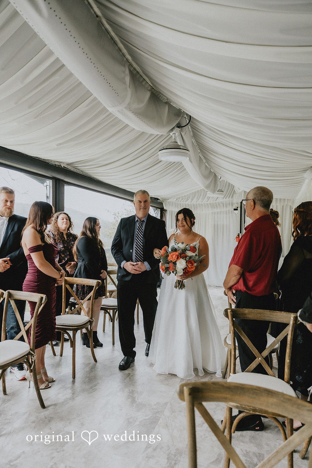 A bride walking down the aisle accompanied by an older man in a suit.