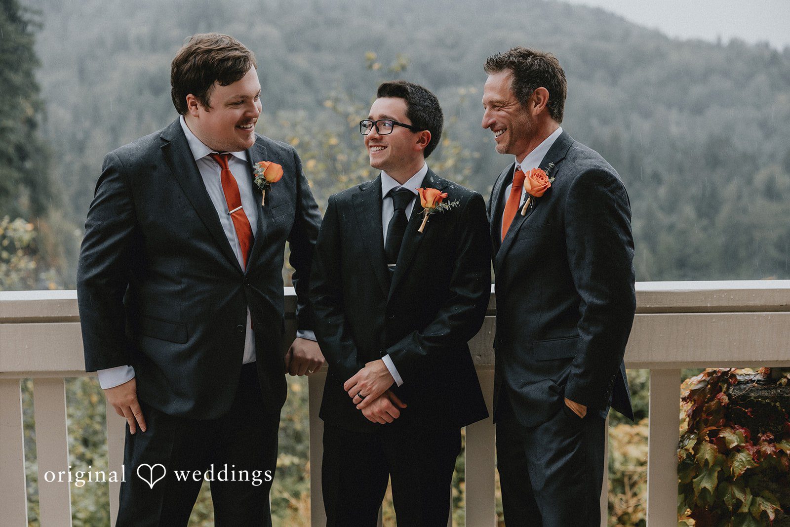 Three men in matching dark suits posing together against a scenic backdrop.