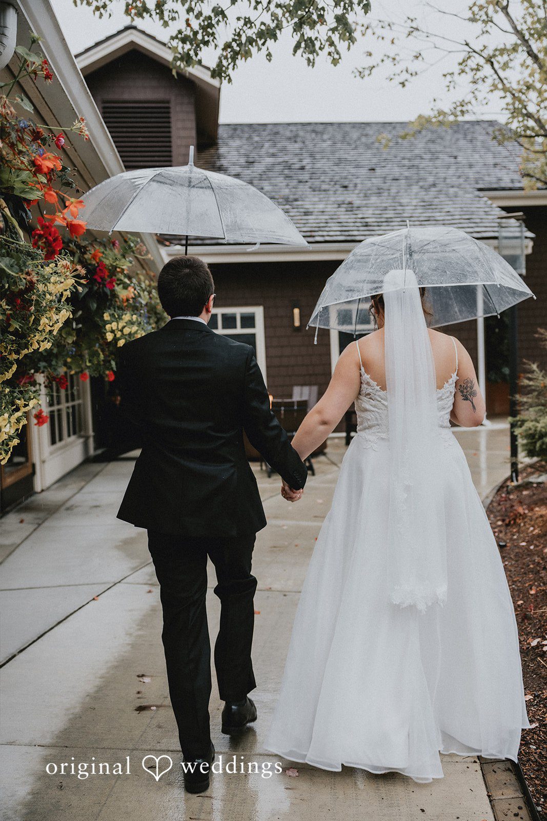 A bride and groom walking together under an umbrella on a path.