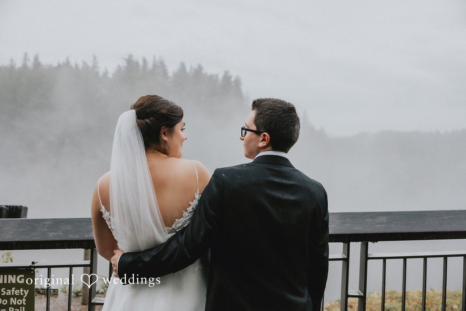 A bride and groom standing closely together while looking out toward a misty landscape.