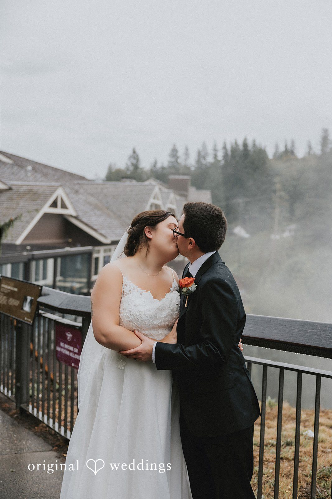 A bride and groom sharing a kiss on a balcony overlooking trees.