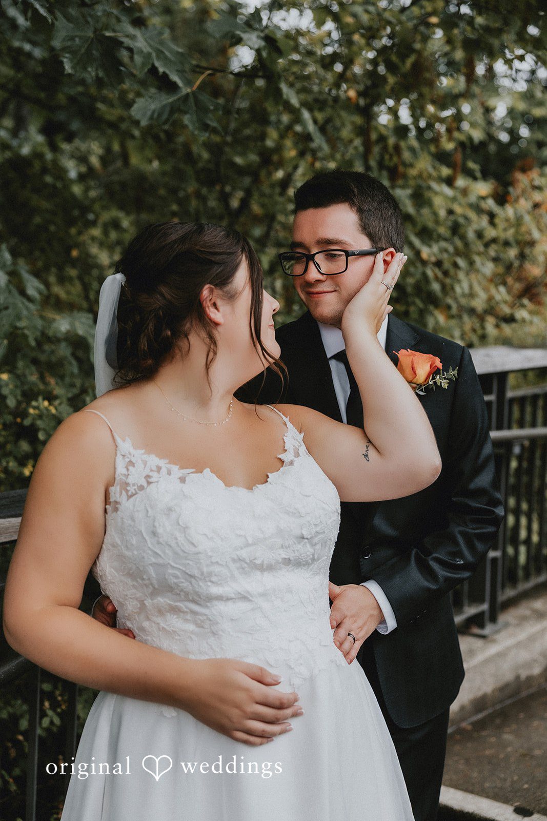 A bride smiling while standing next to a groom in a dark suit.