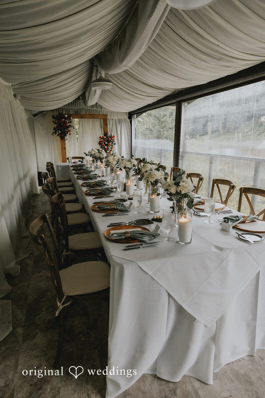 A long dining table set with white linens inside a reception tent.