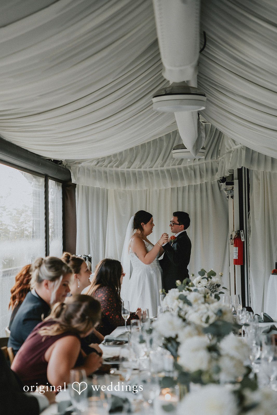 People gathered around tables during a reception dinner inside a tent.