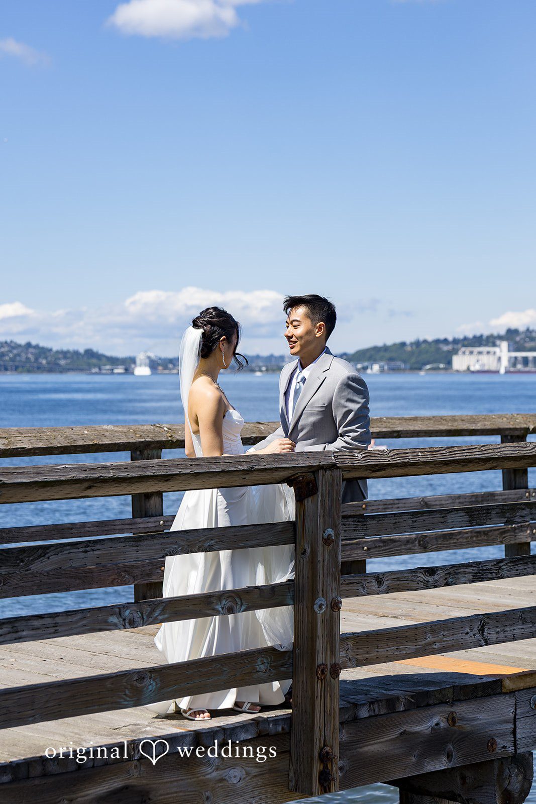 Emily + Paul A bride and groom standing together on a wooden pier overlooking a wide body of water.