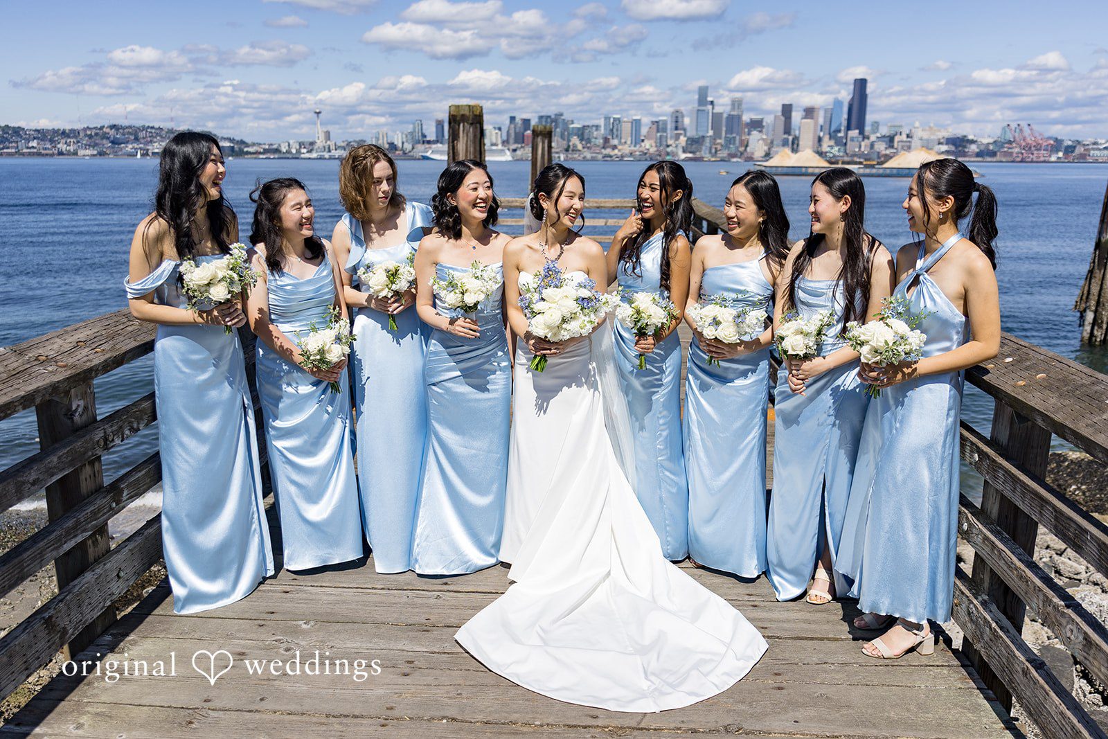 Emily + Paul A bridal party wearing matching blue dresses standing together and smiling on a wooden deck.