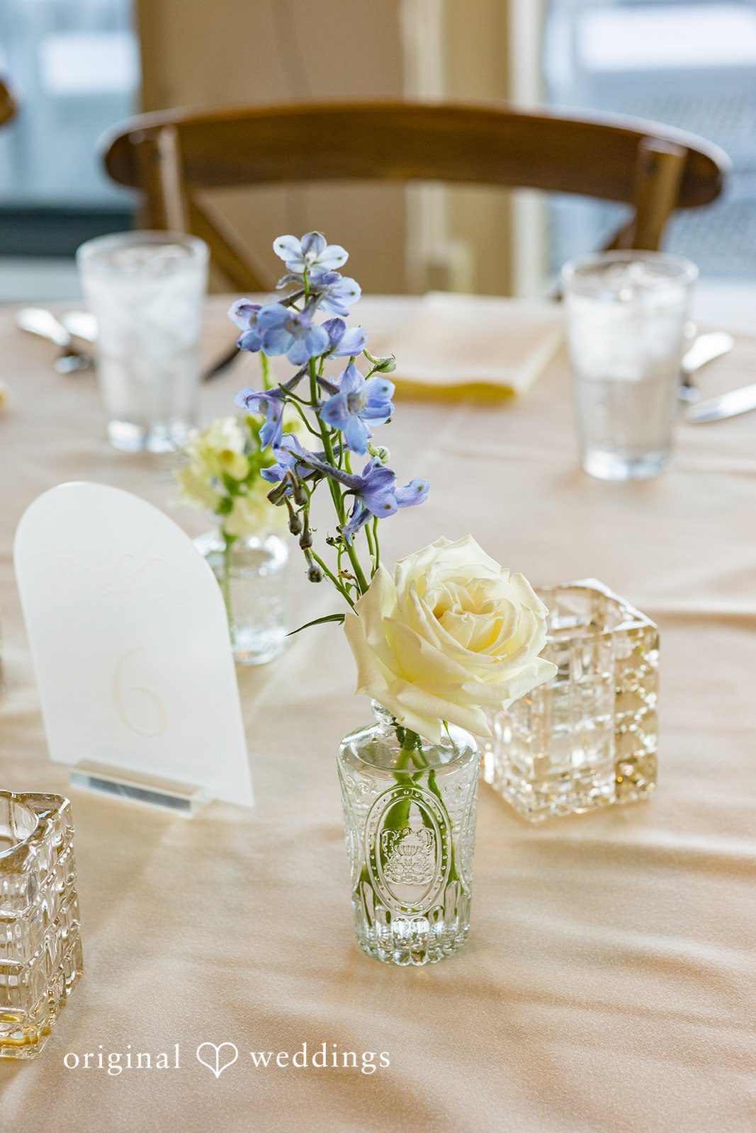 Emily + Paul A close-up of a wooden reception table decorated with delicate blue flowers in small glass vases.