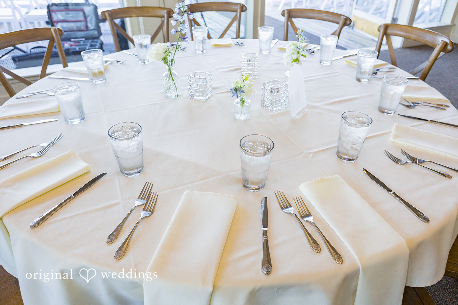 Emily + Paul A round reception table elegantly set with white linens, plates, and formal silverware.