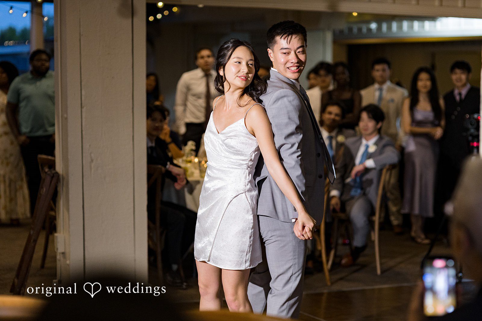 Emily + Paul A bride and groom standing together amidst guests on a dimly lit dance floor.