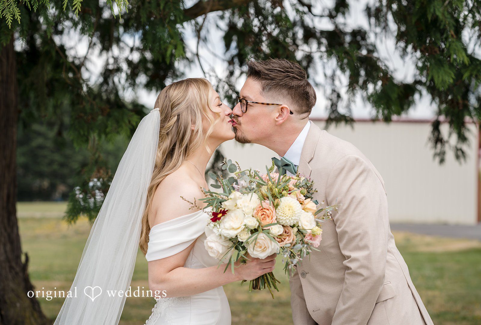 A bride and groom kissing while the bride holds a wedding bouquet.
