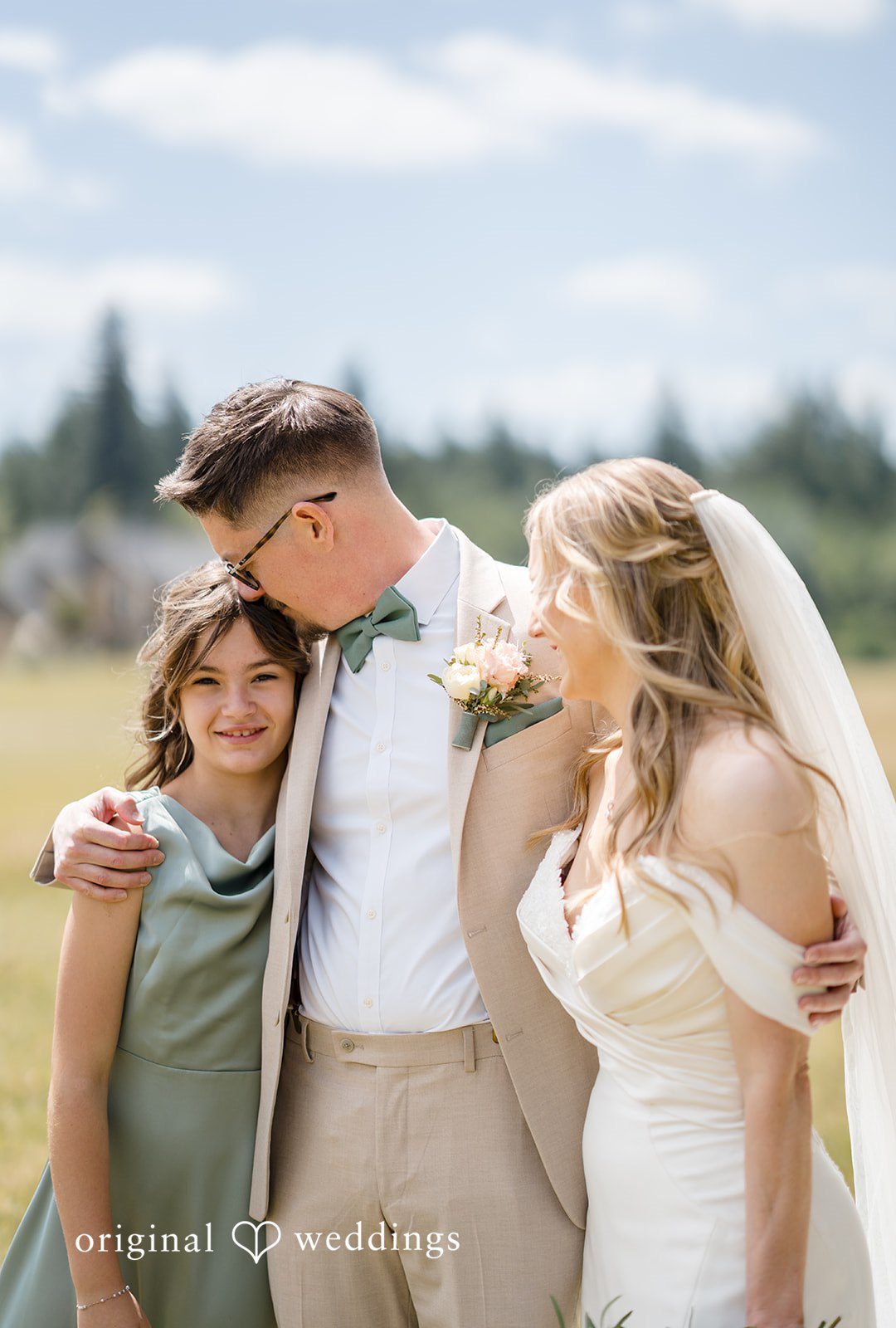 A bride and groom posing and smiling alongside a young wedding guest.