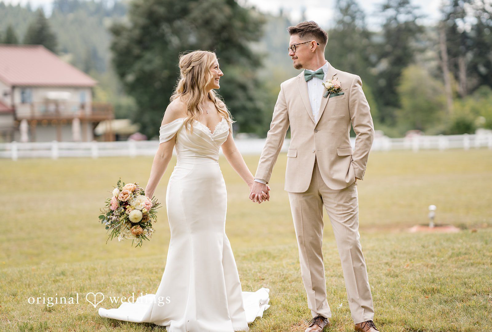A bride and groom holding hands and walking away from a farmhouse structure.