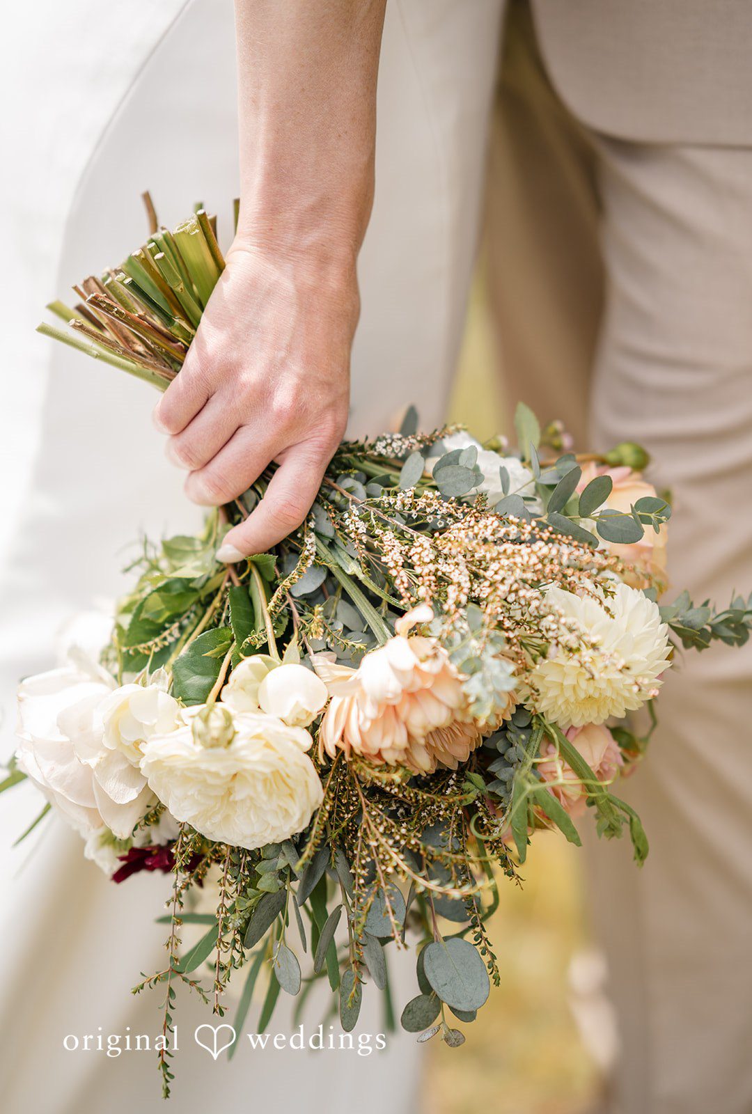 A close-up view of a person holding a large, rustic wedding bouquet.