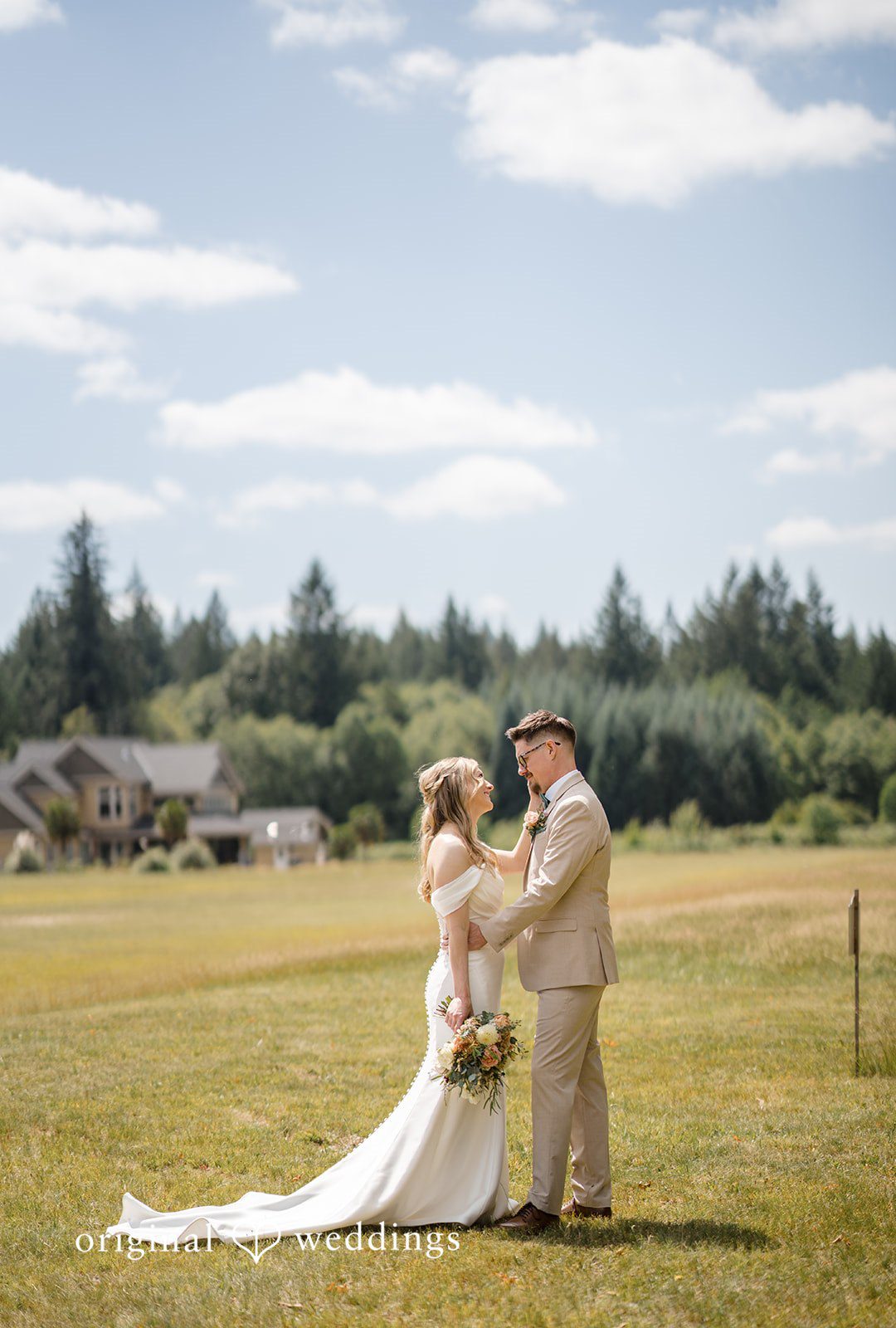 A bride and groom smile at each other while posing in a wide grassy field