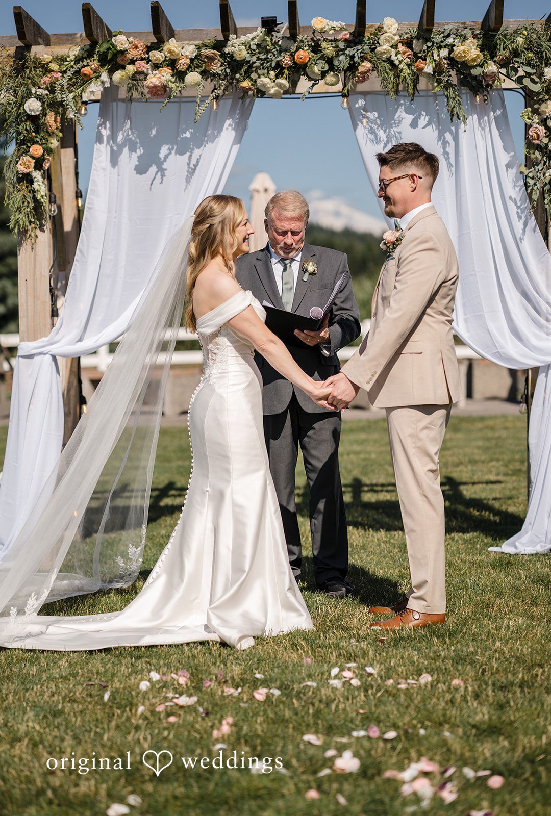 A bride and groom standing hand-in-hand under a decorated wedding arch during their ceremony.
