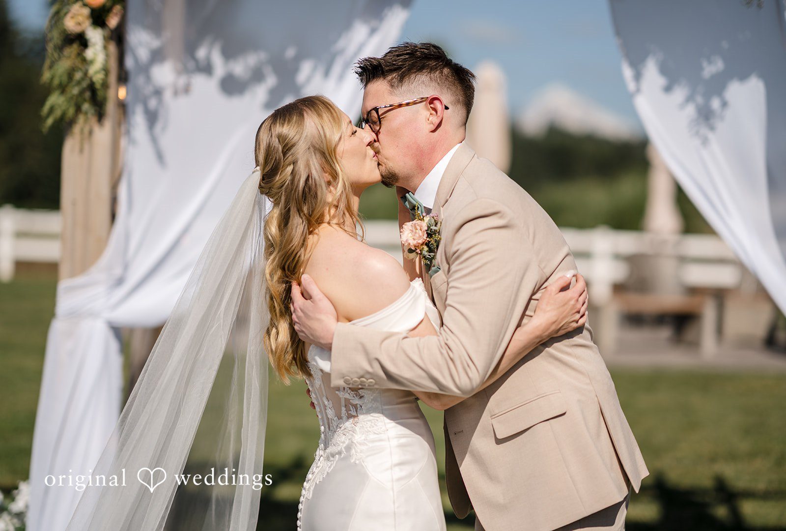 A newly married bride and groom embracing under a fabric canopy.