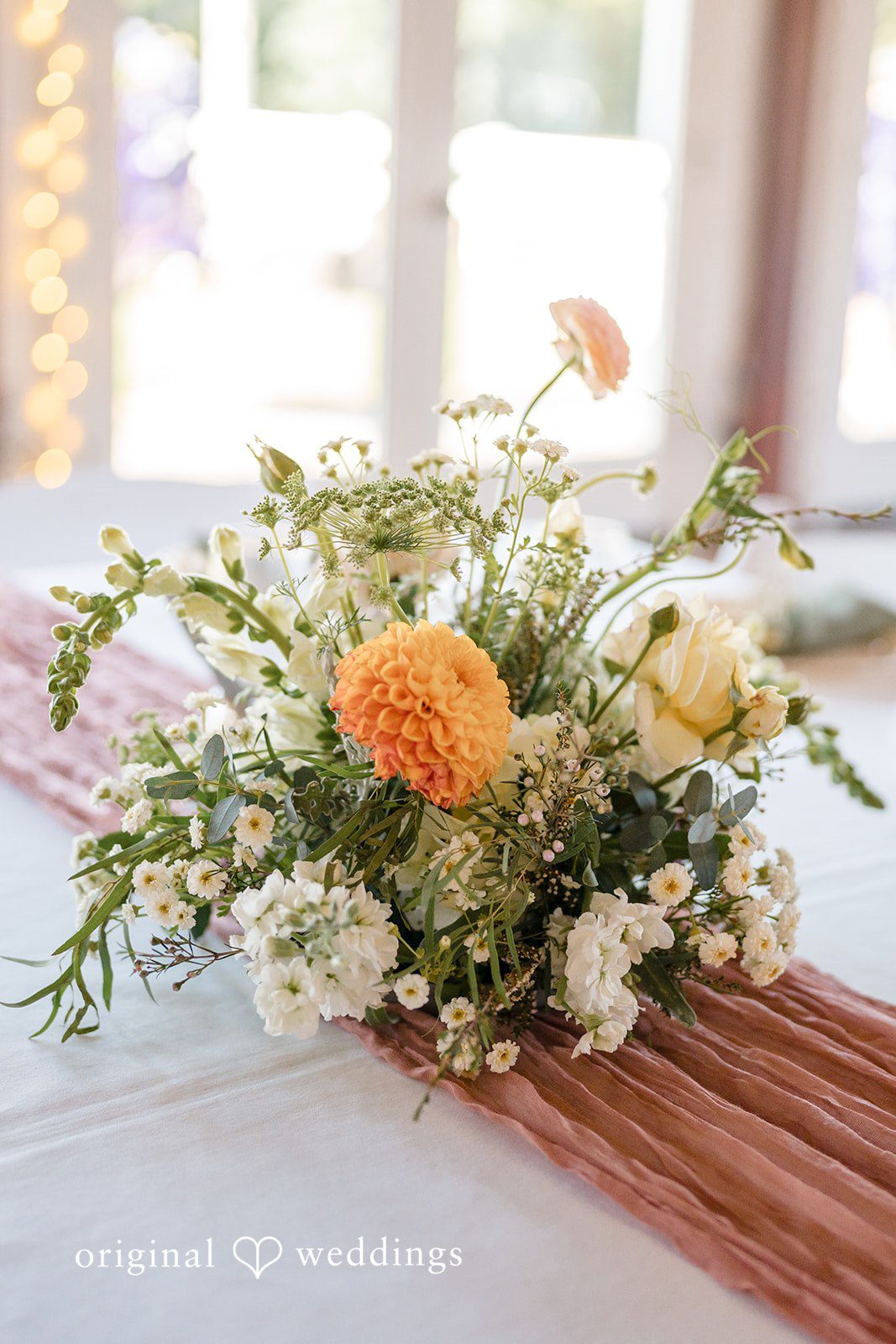 A rustic wedding centerpiece featuring orange and white flowers on a wooden table.