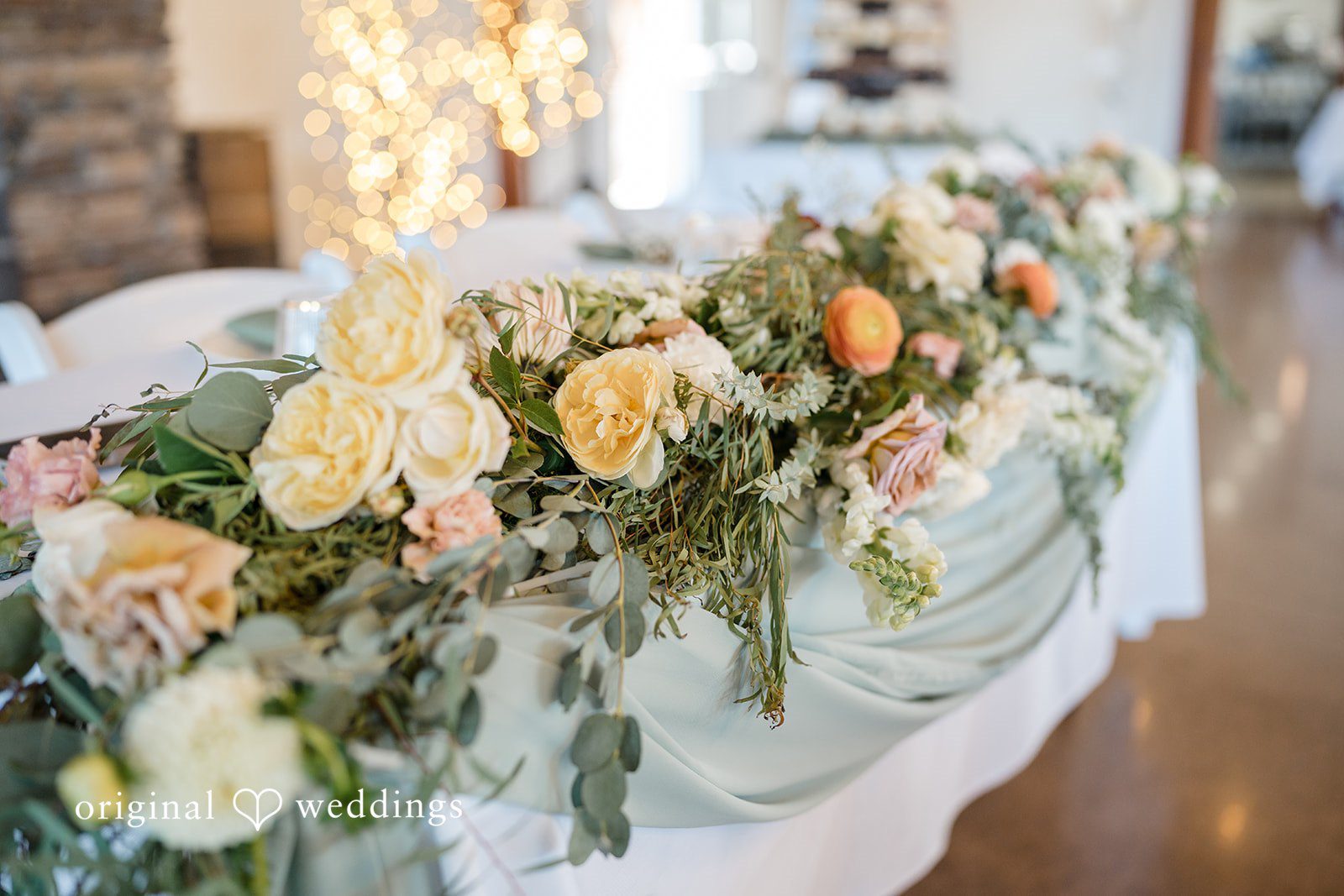 A wedding reception head table decorated with lush green and white floral arrangements.