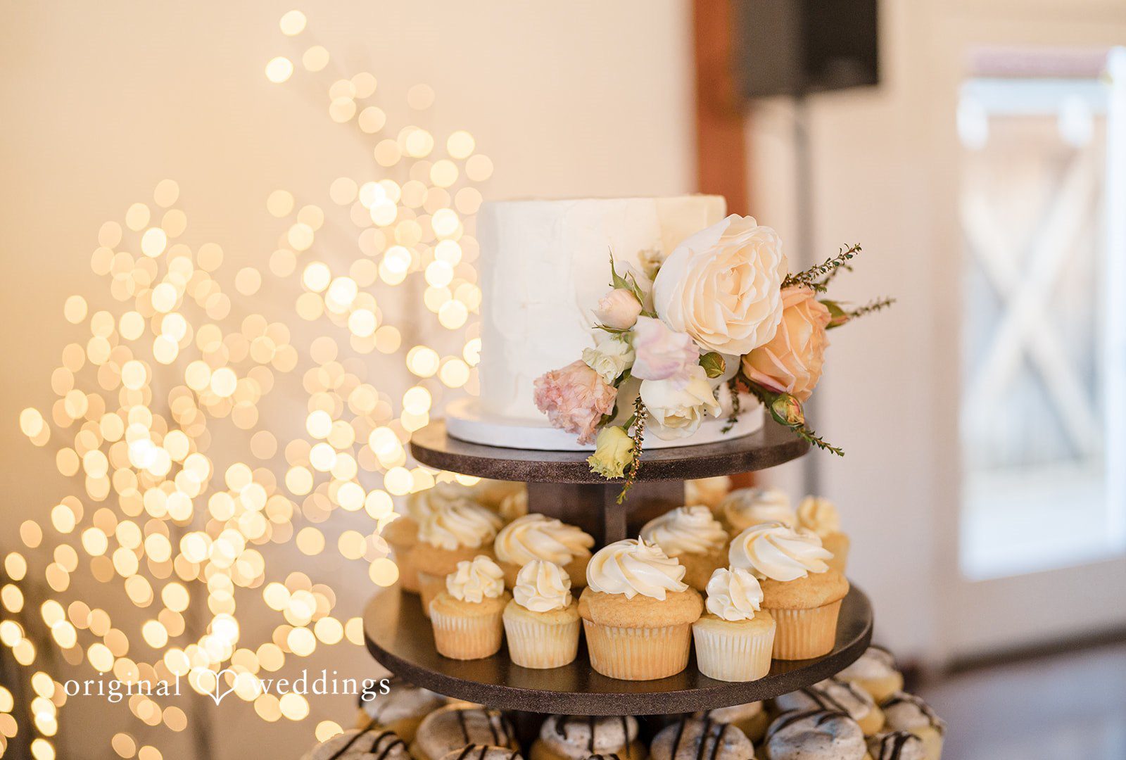 A tiered wedding cake stand surrounded by warm, glowing lights.