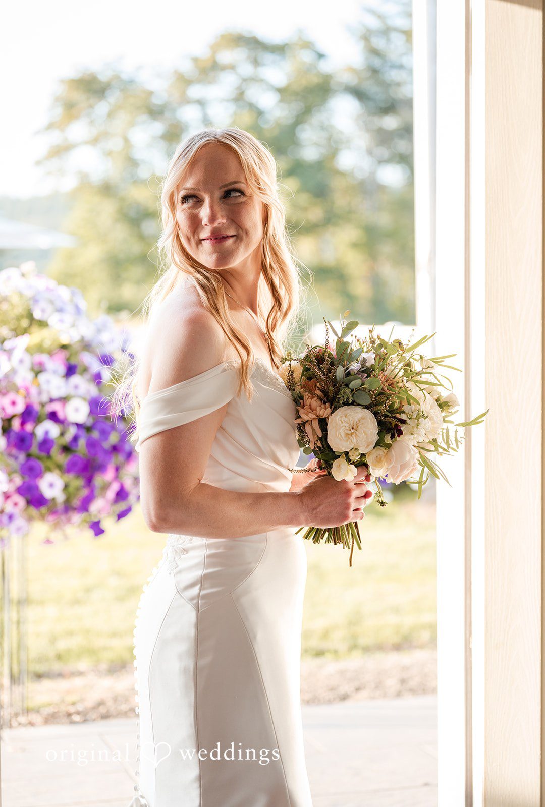 A bride smiling while holding her wedding bouquet.