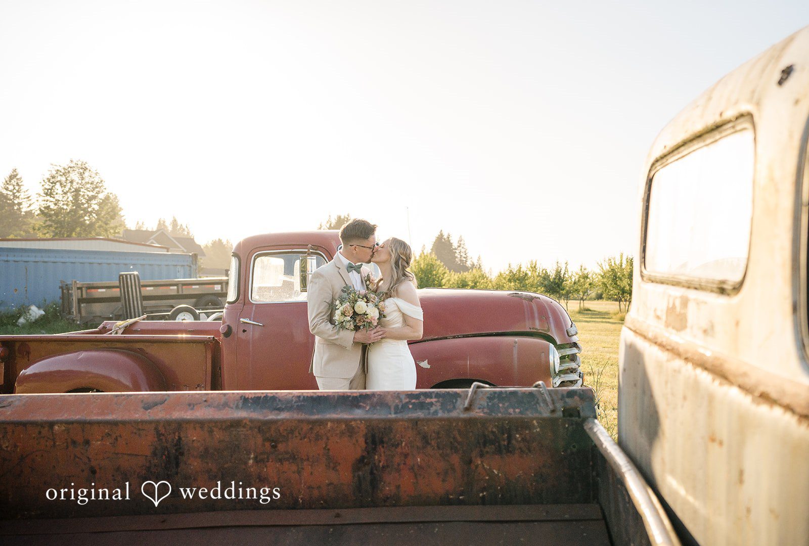 A bride and groom standing in the open bed of a vintage pickup truck.
