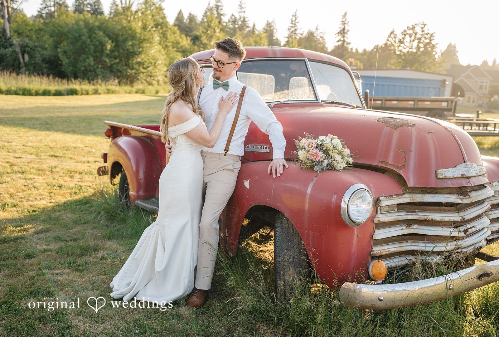 A bride and groom posing together next to a vintage red pickup truck.
