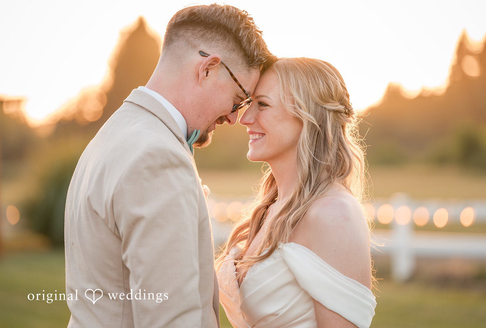 A groom leaning down to touch foreheads with his smiling bride in warm sunlight.