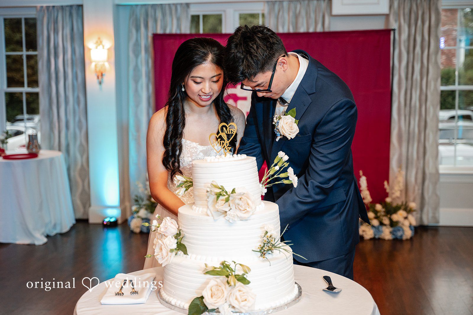 Bride and groom standing together next to a multi-tiered white wedding cake.