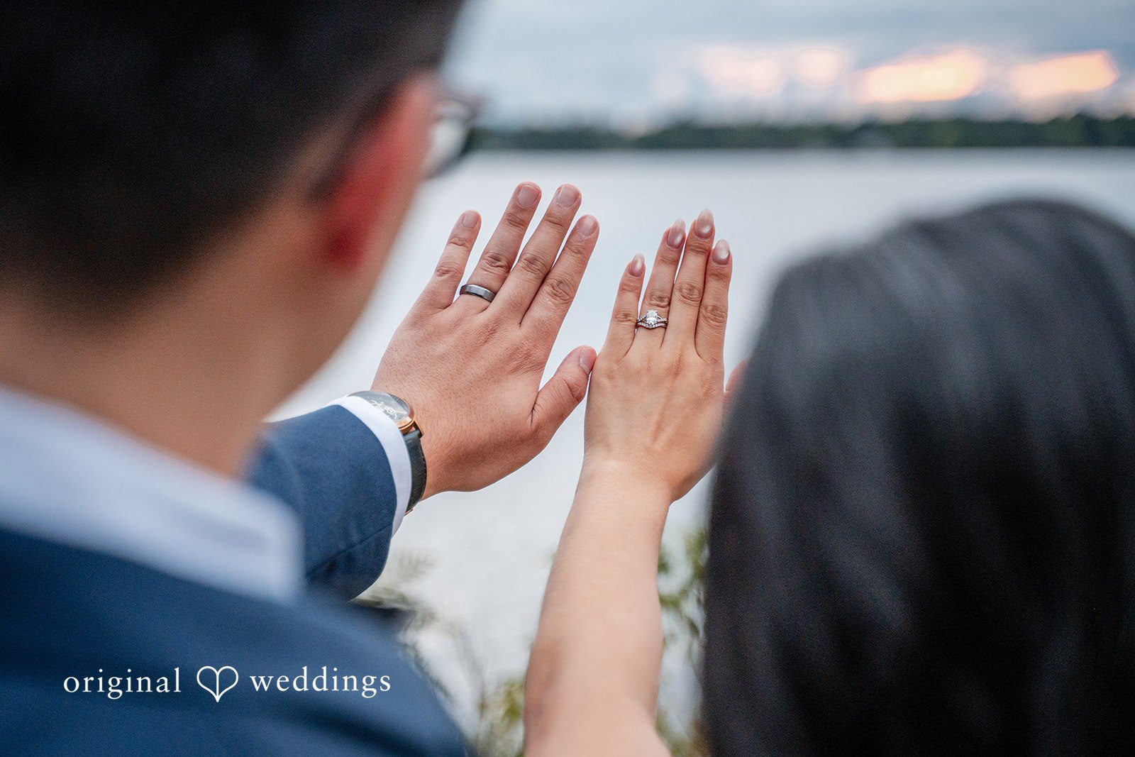 Close-up of a couple's hands held up together with rings visible against a soft background.