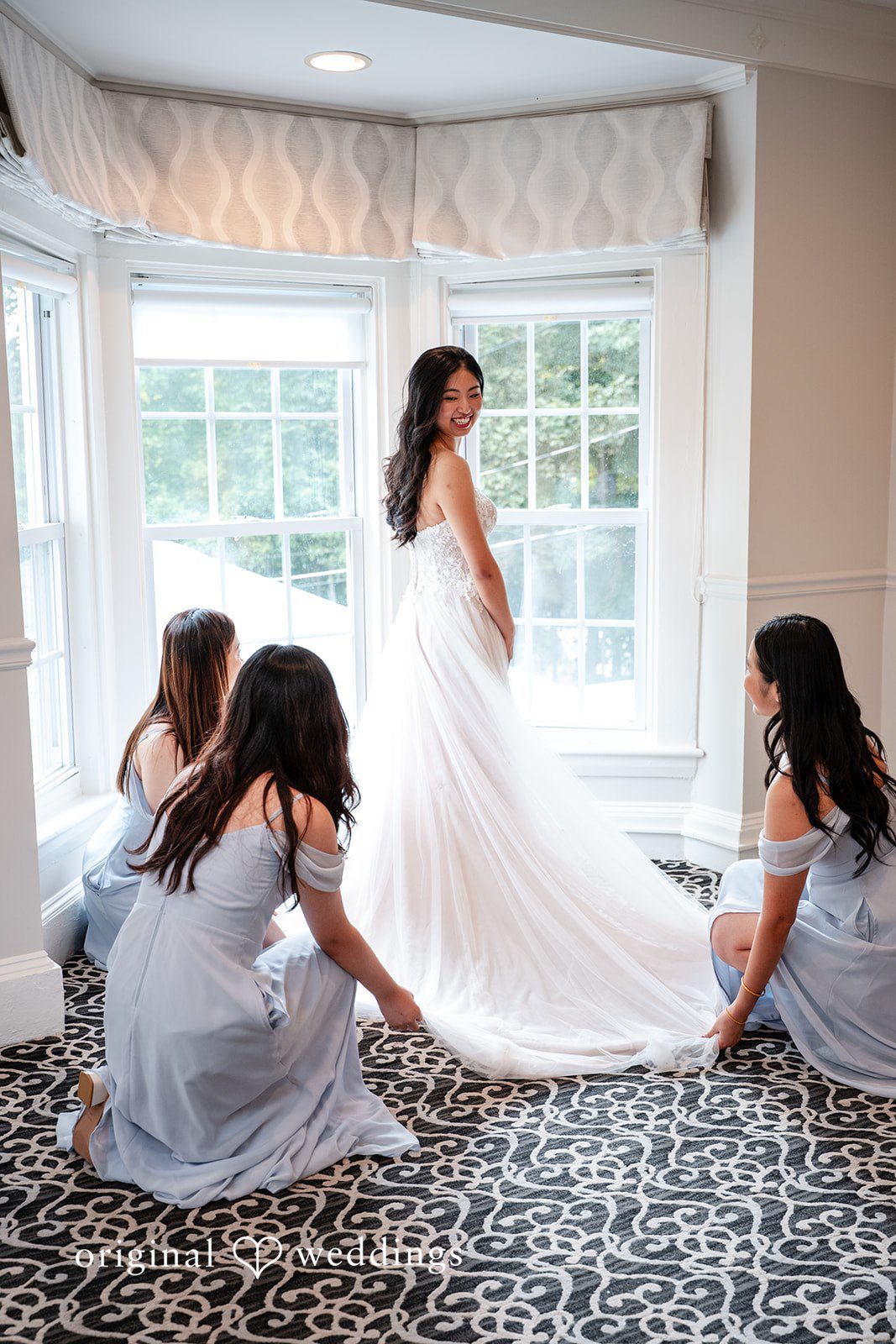 Bride getting ready surrounded by bridesmaids in a brightly lit room.