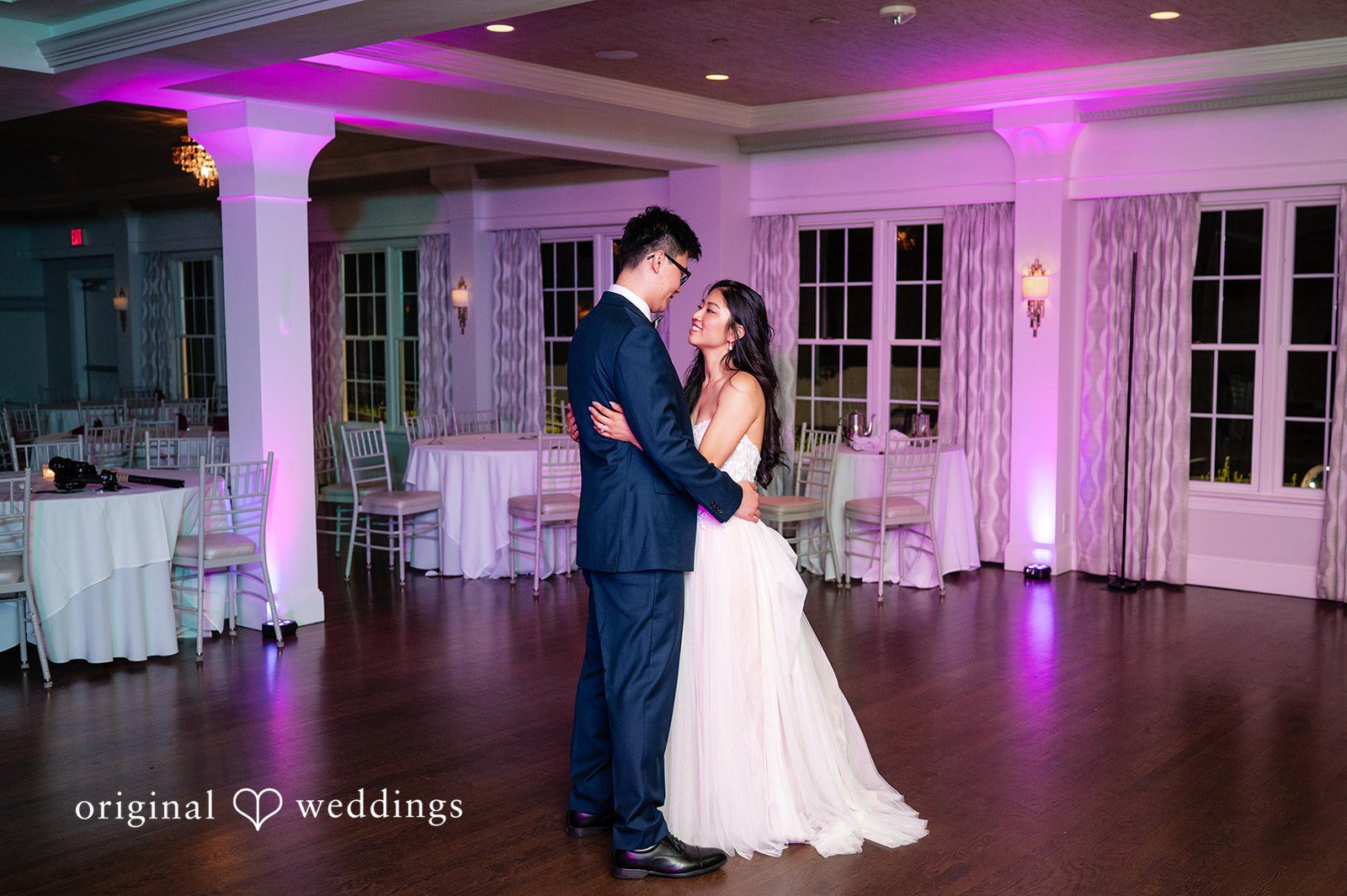 Bride and groom sharing a slow dance under pink reception lighting.