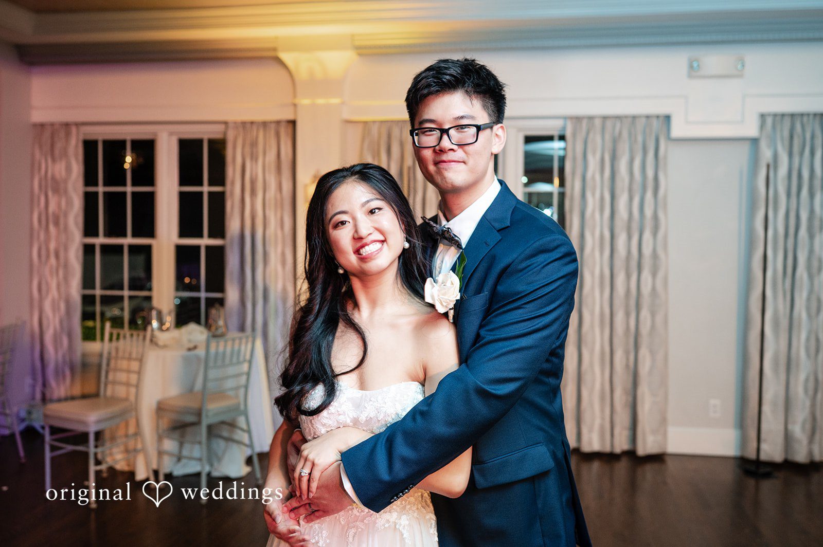 Groom in a blue suit standing closely behind a smiling bride.