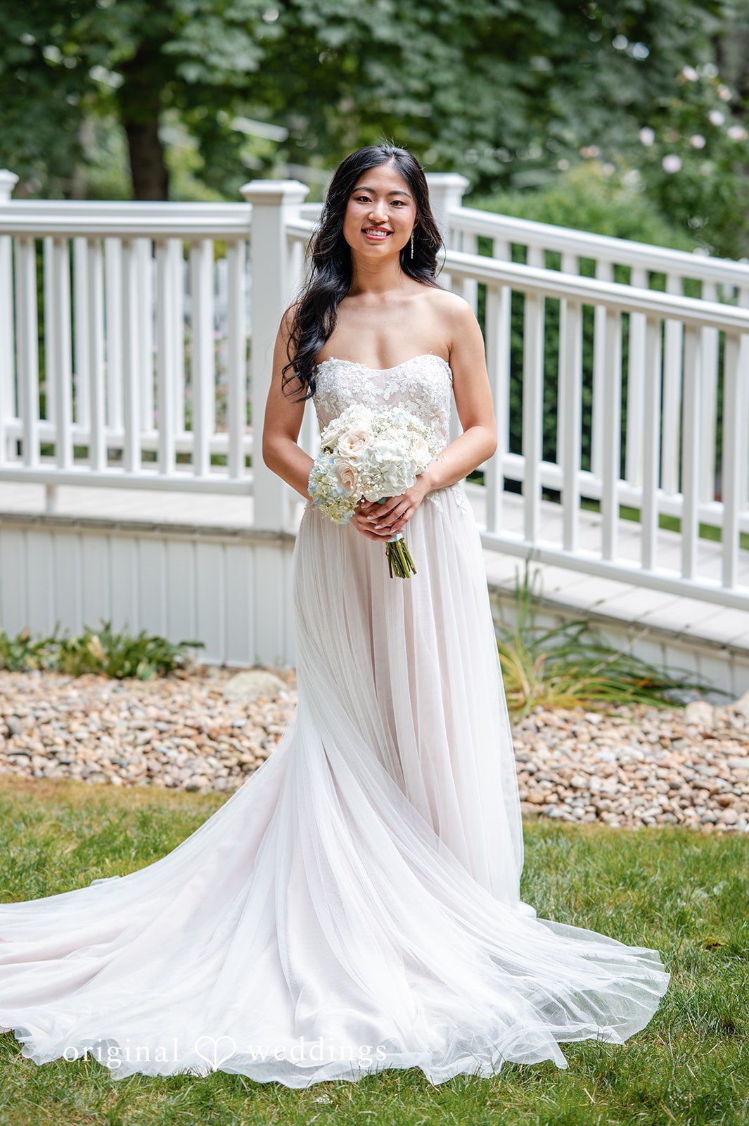 Bride posing in her wedding dress along a white wooden railing.