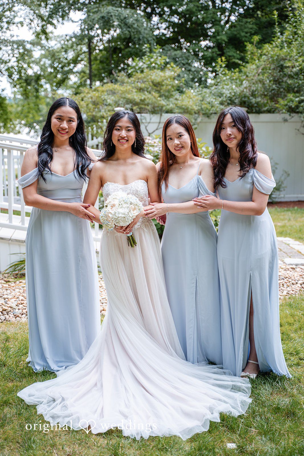 Bride posing on a lawn with bridesmaids wearing light blue dresses.