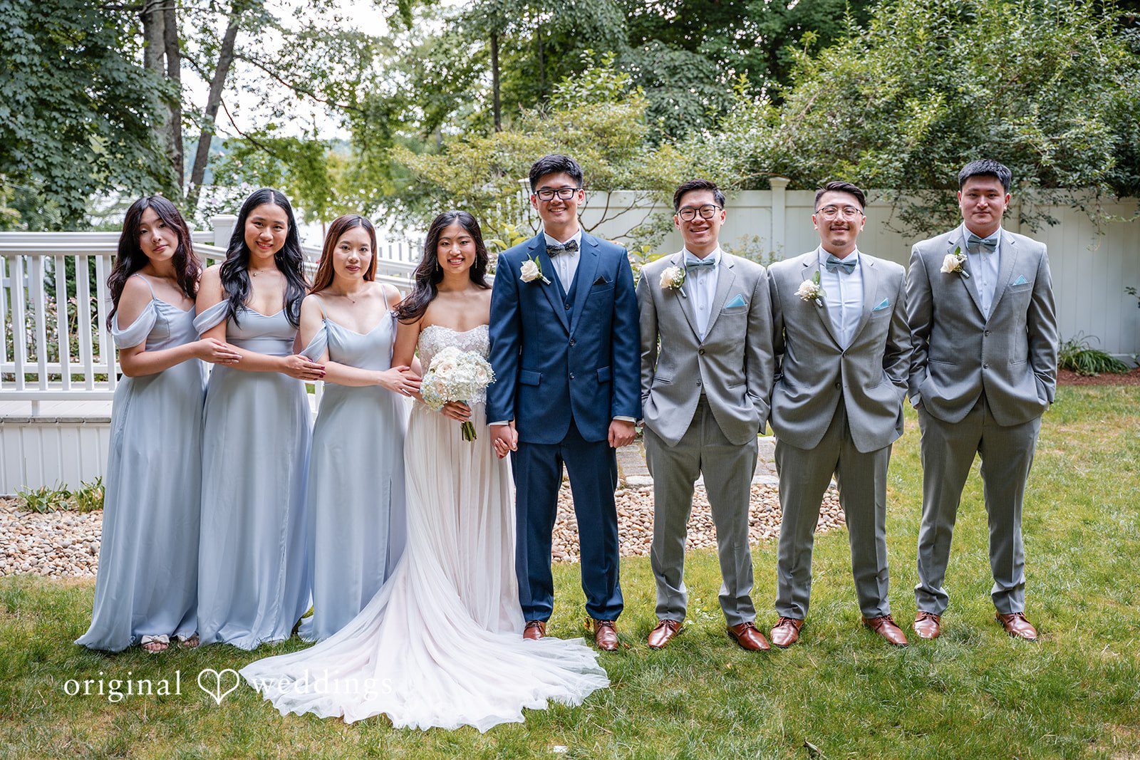 Bride and groom standing with their wedding party on a paved pathway.
