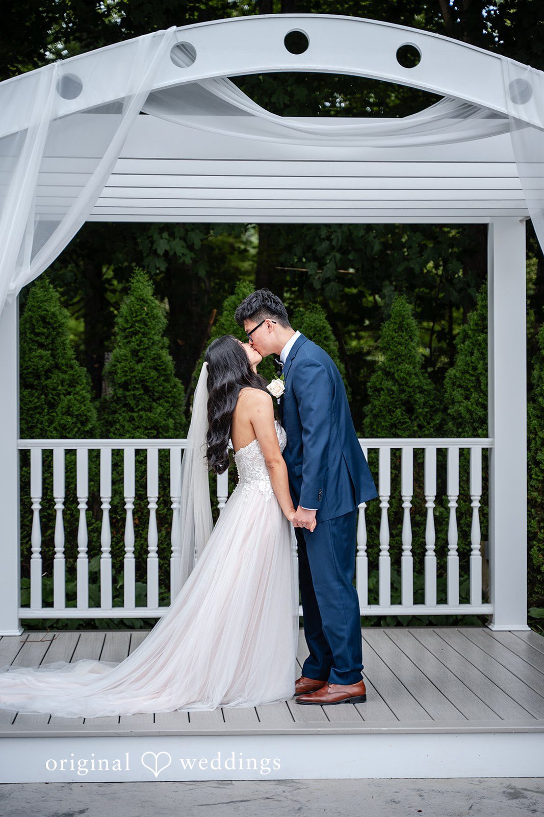 Bride and groom sharing an intimate embrace under a white pavilion structure.
